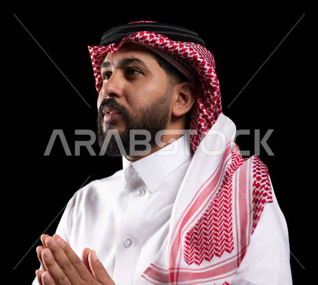 A hand movement indicating supplication and pleading, a request for sympathy and assistance, a portrait of a Saudi Gulf Arab man wearing a shemagh and traditional dress, raising his hand upwards with gestures of supplication and supplication, black background.