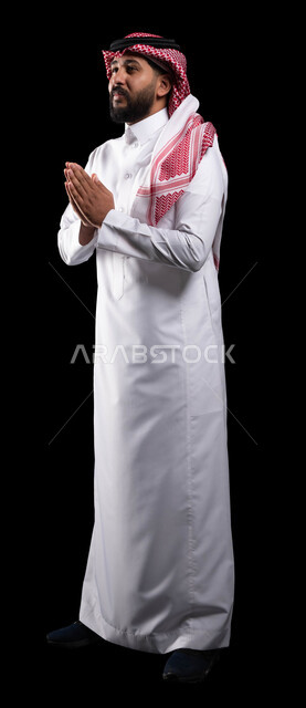 حركة يد تدل على الدعاء والتوسل، بورتريه لمواطن عربي خليجي سعودي يرتدي الشماغ والثوب التقليدي ويرفع يده لاعلى بإيماءات الاسترحام والترجي، طلب العطف والمساعدة، صورة الجسم بالطول الكامل، خلفية سوداء