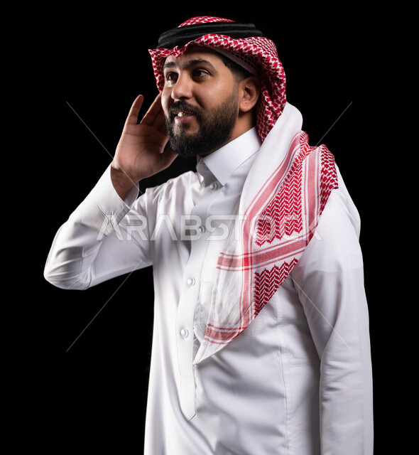 التركيز على الكلام وسماع الاسرار، بورتريه لمواطن عربي خليجي سعودي يرتدي الزي التقليدي ويضع يده خلف أذنه، محاولة والتجسس والتنصت، حسن الاستماع والانصات، خلفية سوداء