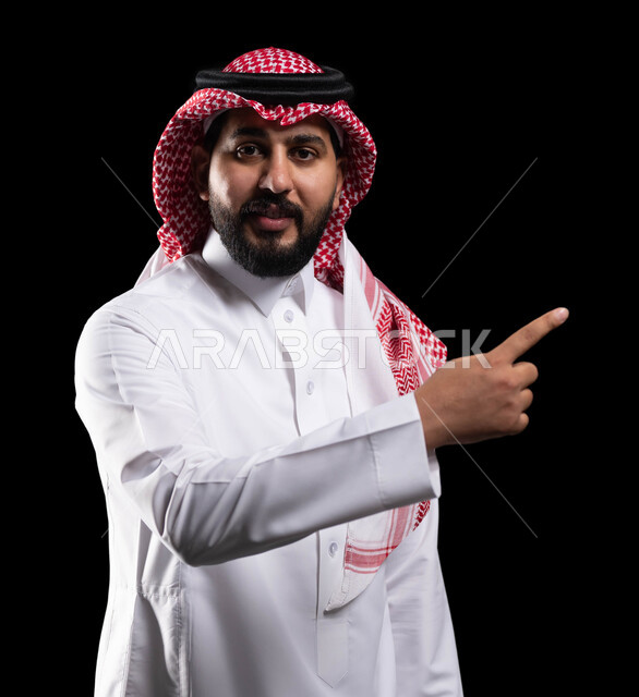 تعابير التأكد والتحديد, الاشارة إلى شيء ما بإيماءات السرور ,بورتريه مقرب لرجل عربي خليجي سعودي مبتسم يرتدي الزي التقليدي والشماغ يشير بأصابع السبابة للاختيار وينظر إلى الكاميرا، خلفية سوداء