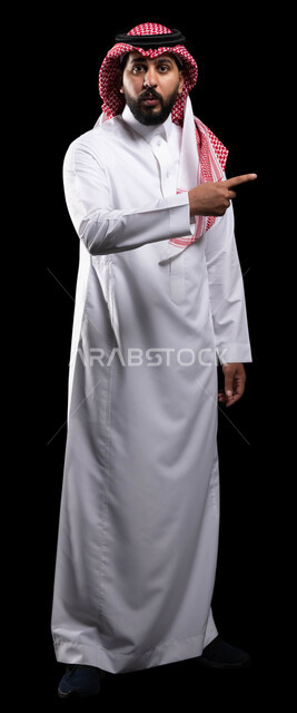 إيماءات الذهول و الصدمة ،التعجب والاستغراب والاندهاش من امر ما، الاشارة نحو شيء وتحديد هدف ما، بورتريه مقرب لرجل عربي خليجي سعودي يرتدي الشماغ والثوب التقليدي ويشير بأصبع السبابة على مكان معين ،صورة الجسم بالطول الكامل، خلفية سوداء