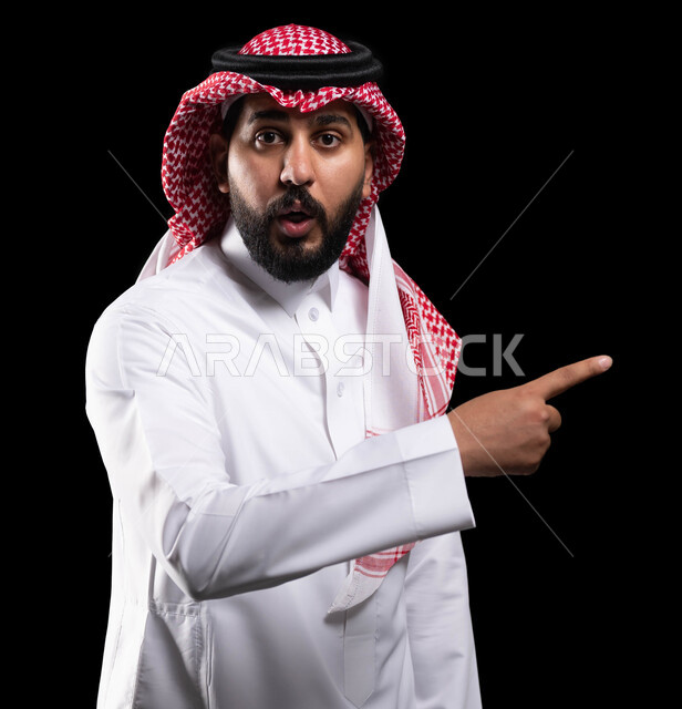 التعجب والاستغراب والاندهاش من امر ما، الاشارة نحو شيء وتحديد هدف ما، بورتريه مقرب لرجل عربي خليجي سعودي يرتدي الشماغ والثوب التقليدي ويشير بأصبع السبابة على مكان معين بإيماءات الصدمة والذهول، خلفية سوداء