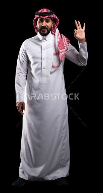 الموافقة والرضا و القبول، التعبير عن الجودة والاتقان، بورتريه لشاب عربي خليجي سعودي يرتدي الثوب التقليدي والشماغ ويشير بيده بإيماءات وتعابير وجه و يدين تدل على الاعجاب، علامة الجودة الامتياز والتميز، صورة لكامل الجسم ،خلفية سوداء
