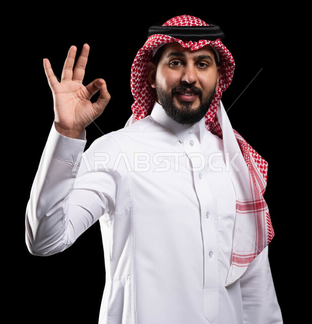 التعبير عن الجودة والاتقان، بورتريه لشاب عربي خليجي سعودي يرتدي الثوب التقليدي والشماغ ويشير بيده بإيماءات وتعابير وجه و يدين تدل على الاعجاب، علامة الجودة الامتياز والتميز، القبول والموافقة والرضا، خلفية سوداء