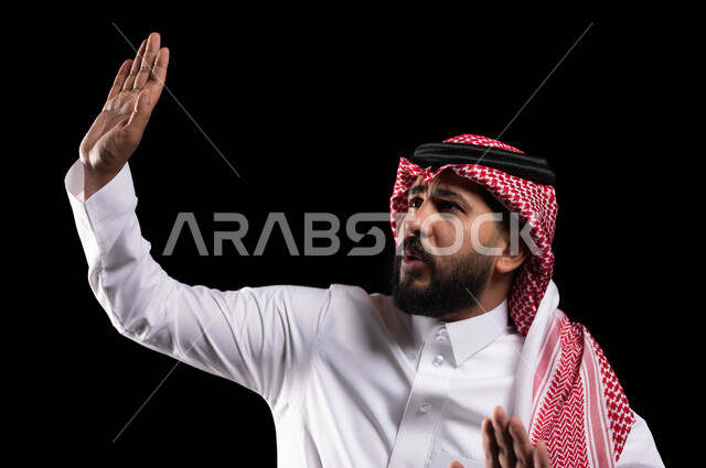 الاحتياط والقلق والابتعاد عن شيء ما, حماية النفس من ضرر خارجي, رفع اليدين بإيماءات التوقف وعدم الاقتراب, بورتريه مقرب لرجل عربي خليجي سعودي يرتدي الثوب التقليدي والشماغ يقف بحذر, خلفية سوداء