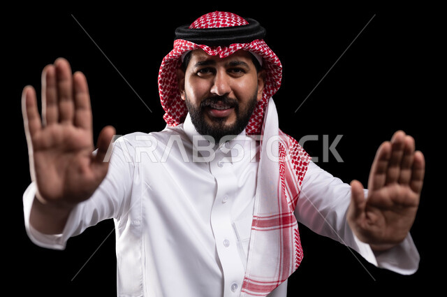 الرعب والذعر والرهبة من شيء ما، بورتريه لرجل عربي خليجي سعودي يرتدي الشماغ والزي التقليدي ويرفع كفيه لأعلى بإيماءات الخوف، طلب التوقف والإمتناع عن فعل شيء ما، حماية النفس من ضرر خارجي, خلفية سوداء