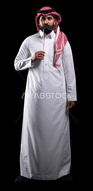 الاهتمام بصحة الرجل، الاحتفال بالمناسبات العالمية، بورتريه لمواطن عربي خليجي سعودي يرتدي الثوب التقليدي والشماغ ويمسك عود خشبي مع قصاصة ورقية على شكل شارب، صورة الجسم بالطول الكامل، اليوم العالمي للرجل 19 نوفمبر، خلفية سوداء
