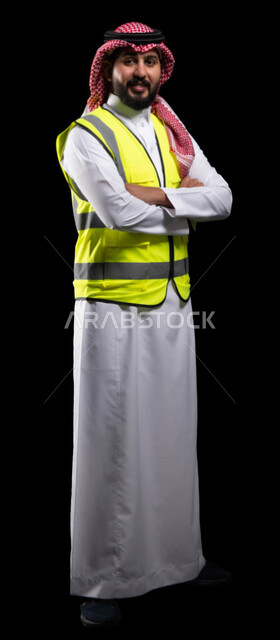مفهوم الهندسة والانشاءات المعمارية، العمل في القطاع الهندسي، بورتريه لمهندس عربي خليجي سعودي مبتسم  سترة الحماية ينظر إلى الكاميرا، الوقوف بإيماءات أيدي متقاطعه، مهن ووظائف سعودية، الإعمار بسواعد أبناء الوطن، صورة الجسم بالطول الكامل، خلفية سوداء