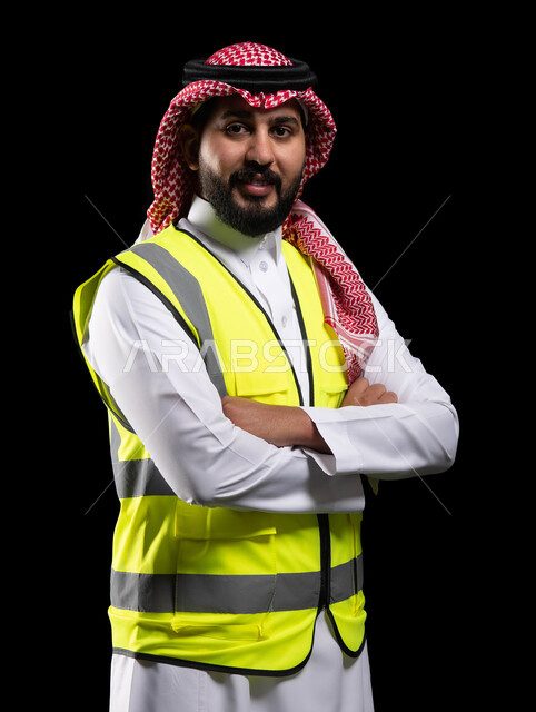 الوقوف بإيماءات أيدي متقاطعه، الرقابة على المشاريع الهندسية و تدقيق الاعمال ،مفهوم الهندسة والانشاءات المعمارية، بورتريه لمهندس عربي خليجي سعودي مبتسم  سترة الحماية ينظر إلى الكاميرا، مهن ووظائف سعودية، الإعمار بسواعد أبناء الوطن، خلفية سوداء