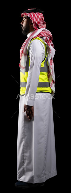Following up on engineering works and plans, reconstruction with the hands of the nation’s people, standing upright and confident, a side portrait of a professional Saudi Arabian Gulf engineer wearing traditional uniform and a protective jacket for work, the concept of engineering and construction, full-length body image, black background