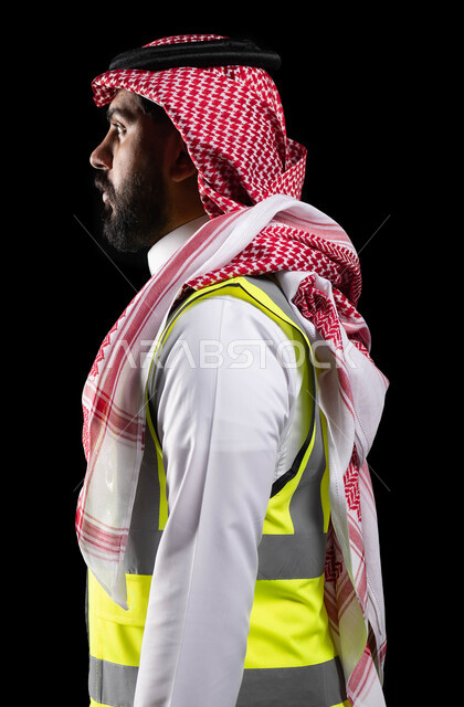 الإعمار بسواعد أبناء الوطن ، متابعة الأعمال والمخططات الهندسية ،الوقوف باستقامة وثقة، بورتريه من الجانب لمهندس عربي خليجي سعودي محترف يرتدي الزي التقليدي وسترة الحماية الخاصة بالعمل، مفهوم الهندسة و الانشاءات، خلفية سوداء
