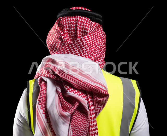 التقدم والتطور في المجال الهندسي السعودي، بورتريه من الخلف لمهندس عربي خليجي سعودي يرتدي الشماغ وسترة الحماية الخاصة بالعمل، العمل في المجال الهندسي، متابعة المشاريع وتدقيق العمل، الوظائف الهندسية في الشركات السعودية، خلفية سوداء