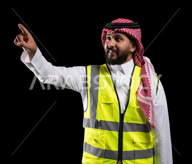 متابعة العمل والاشراف عليه، النقر والضغط على عنصر ما، بورتريه مقرب  لمهندس معماري عربي خليجي سعودي يرتدي الشماغ والثوب التقليدي وسترة الحماية الخاصة بالعمل، الاشارة باصبع السبابة باتجاه ما، الوظائف الهندسية في الشركات السعودية، خلفية سوداء