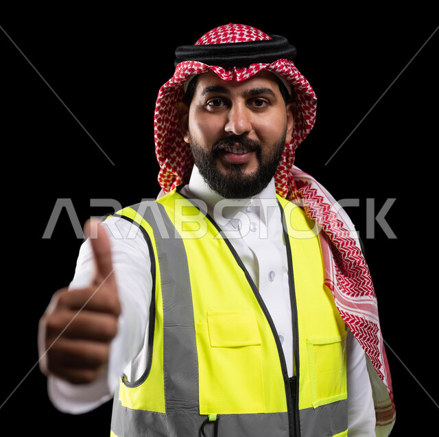 دعم وتنمية القطاع الهندسي، ادارة ومتابعة المشاريع الهندسة، مهن ووظائف سعودية، بورتريه مقرب لمهندس عربي خليجي سعودي يرتدي الزي التقليدي وسترة الحماية الخاصة بالعمل، رفع اصبع الابهام للأعلى بإيماءات القبول والموافقة والاعجاب، خلفية سوداء
