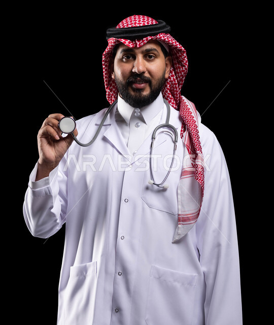 استخدام سماعة الطبيب لسماع نبضات القلب، مفهوم الطب والرعاية الصحية، إجراء الفحوصات اللازمة، بورتريه لطبيب عربي خليجي سعودي مبتسم يرتدي الزي التقليدي والمعطف الطبي، تقديم الخدمات الصحية للمرضى، العمل في المستشفيات والمراكز الطبية السعودية، خلفية سوداء