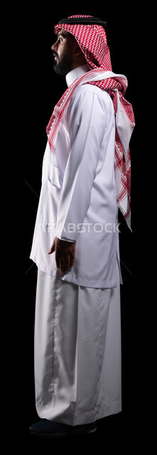مفهوم الطب والرعاية الصحية، مهن ووظائف سعودية، الوقوف باستقامة بإيماءات البحث عن شيء ما  في الجيوب ، بورتريه من الجانب لطبيب عربي سعودي خليجي يرتدي الثوب التقليدي و المعطف الطبي يعمل في القطاع الصحي، مهن ووظائف سعودية ،صورة الجسم بالطول الكامل، خلفية سوداء