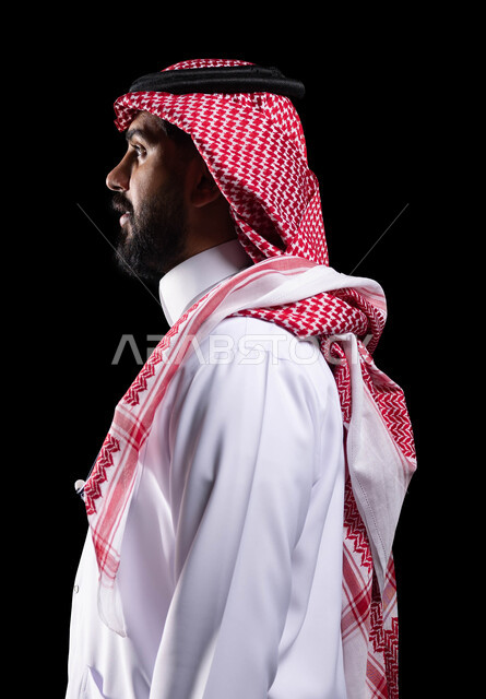 مفهوم الاناقة والاهتمام بالمظهر الخارجي، التخاطب و التحدث مع أحد ما، بورتريه مقرب من الجانب لرجل عربي سعودي خليجي يرتدي الزي التقليدي والشماغ،النظر إلى شيء ما،  خلفية سوداء