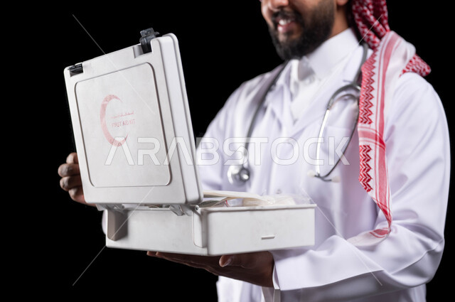 تفقد الأدوات والمعدات الطبية اللازمة، مفهوم الطب و تقديم الخدمات الصحية الطارئة للمرضى، التعامل مع الإصابات الشائعة وحالات الطوارئ، بورتريه مقرب لطبيب عربي سعودي خليجي يرتدي الثوب التقليدي و المعطف الطبي يحمل بيده حقيبة الاسعافات الأولية، خلفية سوداء