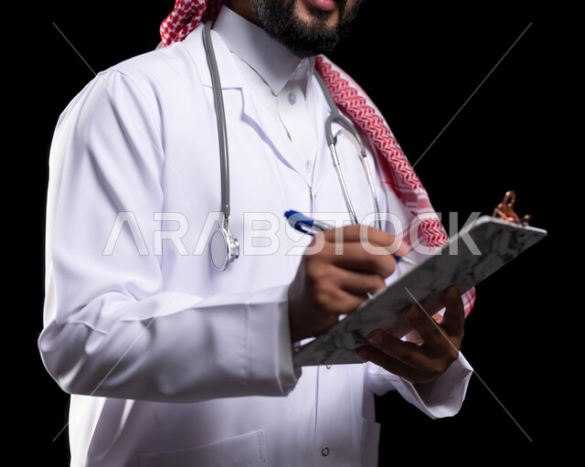 مهن ووظائف سعودية، دراسة و مراجعة حالات المرضى، بورتريه مقرب لطبيب عربي خليجي سعودي يرتدي الزي التقليدي والمعطف الطبي يقوم بتسجيل البيانات على ملف المريض، العمل في القطاع الصحي، إعداد التقارير الطبية، خلفية سوداء