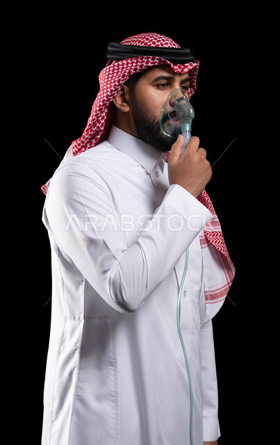 Treating chest diseases, providing comfort to the respiratory muscles using a respirator, a portrait of a Saudi Gulf Arab man wearing a shemagh and traditional dress, inhaling cough medicine, providing home health services to the patient, black background