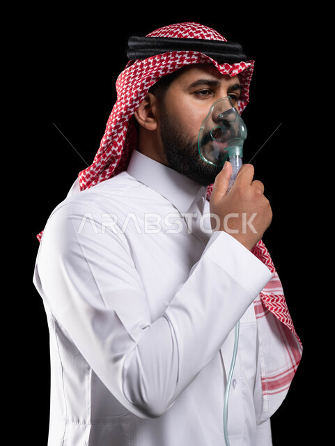 تقديم الخدمات الصحية المنزلية للمريض، معالجة حالات ضيق التنفس، تأمين الراحة للعضلات التنفسية باستخدام جهاز التنفس الصناعي، بورتريه مقرب لرجل عربي سعودي خليجي يرتدي الشماغ والثوب التقليدي يقوم باستنشاق أدوية الكحة ،خلفية سوداء