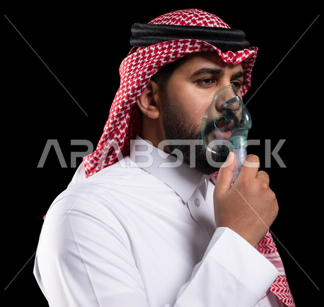 تأمين الراحة للعضلات التنفسية باستخدام جهاز التنفس الصناعي، بورتريه مقرب لرجل عربي سعودي خليجي يرتدي الشماغ والثوب التقليدي يقوم باستنشاق أدوية الكحة ،معالجة حالات ضيق التنفس، تقديم الخدمات الصحية المنزلية للمريض، خلفية سوداء