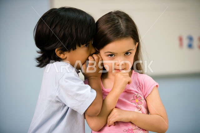 الهدوء والهمس أثناء الكلام, المحافظة على كتمان السر والتحدث بصوت منخفض, إخبار الأسرار للأصدقاء, مشاركة الأخبار السرية لزملاء المدرسة, صورة مقربة لولد عربي خليجي إماراتي يقوم بمشاركة سر ما لصديقته