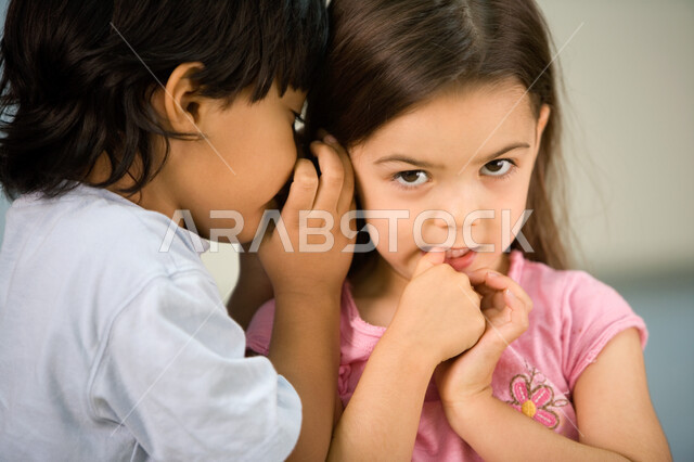 المحافظة على كتمان السر والتحدث بصوت منخفض, إخبار الأسرار للأصدقاء, مشاركة الأخبار السرية لزملاء المدرسة, صورة مقربة لولد عربي خليجي إماراتي يقوم بمشاركة سر ما لصديقته, الهمس والهدوء أثناء الكلام