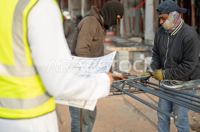 Skill and precision in completing tasks, work in the engineering field, a group of workers preparing steel iron, a close-up photo from the back of a Saudi Arabian Gulf engineer wearing a protective vest holding the construction plan at the construction site, supervising the implementation of engineering projects and plans