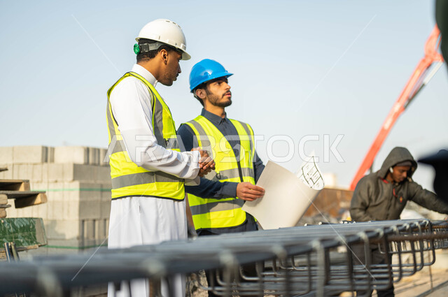 النظر إلى شيء ما بإيماءات التركيز, مهندسان عربيان سعوديان خليجيان يرتديان الستره وخوذه الحمايه يقفان في موقع العمل, الاهتمام بالأساسيات الجيده للمبنى, متابعه سير الخطة التنظيميه للمشروع, النقاش والحوار وتبادل الأفكار, التحقق من تطبيق الشروط الصحيحه للبناء