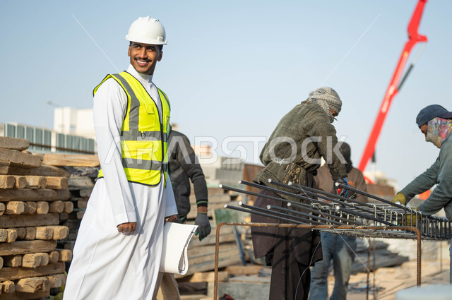 المهاره والدقه في اتقان العمل, النمو والتطور العمراني بسواعد أبناء الوطن, مهن ووظائف سعوديه, مجموعه من العمال يقومون بتجهيز وقص الحديد الصلب بمعدات وأدوات البناء, مهندس عربي خليجي سعودي مبتسم يرتدي الستره وخوذه الحمايه ينظر إلى شيء ما بإيماءات السرور