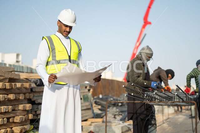 الدقه والمهاره في اتقان العمل, مهن ووظائف سعوديه, مجموعه من العمال يقومون بتجهيز وقص الحديد الصلب بمعدات وأدوات البناء, مهندس عربي خليجي سعودي يرتدي الستره وخوذه الحمايه ينظر إلى مخطط الرسومات والإنشاءات الهندسيه