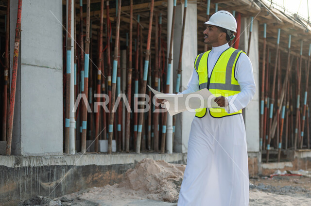 Working in the engineering sector, a Saudi Gulf Arab engineer wearing a helmet and a protective vest holds an organization plan in his hand, looking at something and verifying the application of architectural projects and plans in construction in Saudi Arabia, making sure to build good basics for the building.