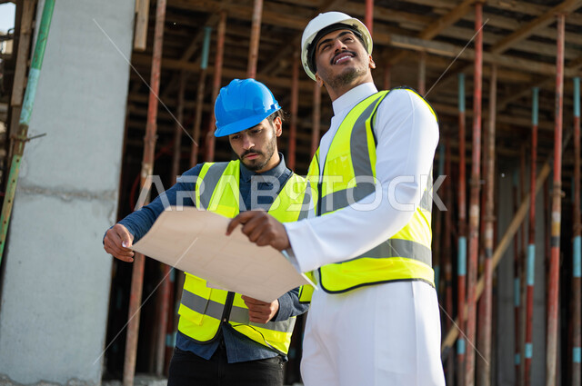 الاشراف على تطبيق المشاريع و الخطط الهندسيه المعمارية في البناء, مشاورات في إنجاز العمل واقتراح افكار جديده, عامل ومهندس معماري عربيان سعوديان خليجيان يرتديان الخوذه وستره الحماية يمسكان مخطط المشروع, العمل في القطاع الهندسي