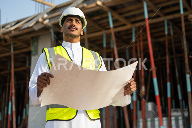 مهن ووظائف سعوديه,  الدقه والمهاره في إتقان العمل ,  مهندس عربي خليجي سعودي يرتدي الستره وخوذه الحمايه يحمل بيده مخطط الرسومات والإنشاءات الهندسيه وينظر نحو الأعلى , معاينة تطبيق الخطط والمشاريع الأساسية للمباني , إيماءات التركيز والاهتمام .