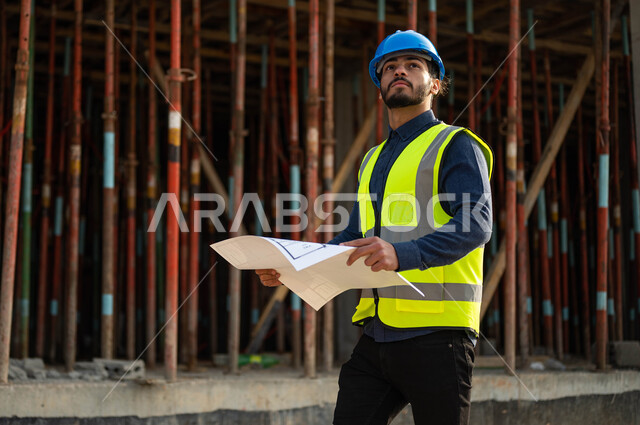 النظر إلى الأعلى بإيماءات التدقيق والاهتمام, صورة مقربة لمهندس عربي خليجي سعودي يرتدي الخوذة وسترة الحماية ويحمل بيده مخططات البناء, العمل في القطاع الهندسي العمراني, التحقق من تطبيق المشاريع والخطط الهندسيه المعمارية, معاينة الأساسيات الجيده للمباني .