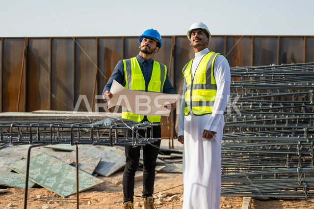 تبادل الأفكار والآراء لتطوير العمل الهندسي  , المشاركة و النقاشات حول مشروع العمل، الاهتمام في بناء الأساسيات الجيده للمباني، متابعة سير المشاريع الإعمارية, مهندسان عربيان خليجيان سعوديان يرتديان الخوذة وسترة الحماية في موقع المشروع .