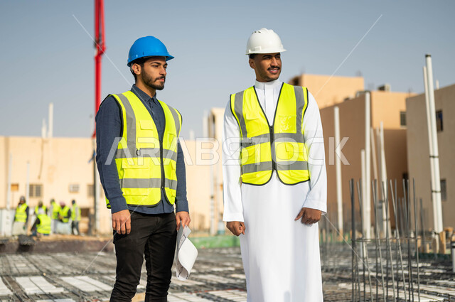 Construction construction in Saudi territory, following up on the progress of construction projects, making sure to build good basics for buildings, two Saudi Gulf Arab workers and engineers wearing helmets and protection vests and standing at the work site