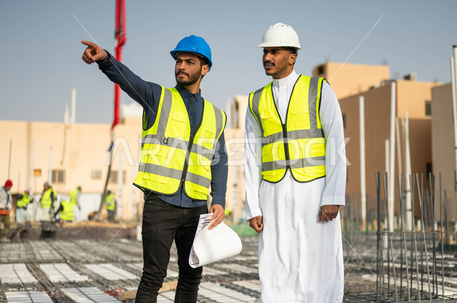 Gestures of focus and pointing to something, following up on the progress of construction projects and verifying the implementation of architectural plans, making sure to build good basics for buildings, a Saudi Gulf Arab worker and engineer wearing a helmet and a protective vest at the work site