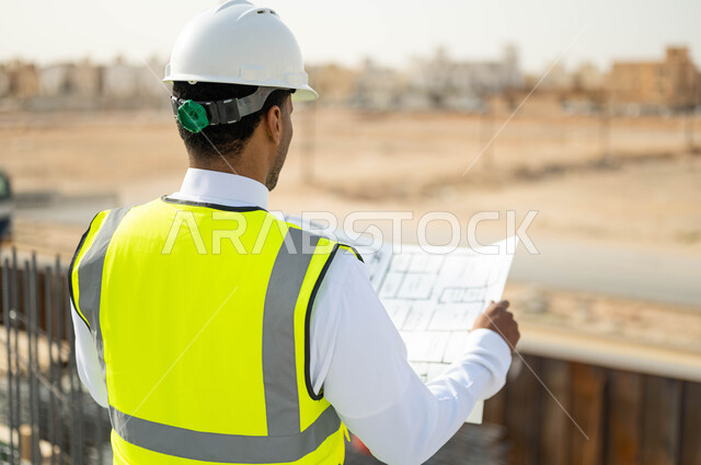 تصاميم معمارية حديثة, الرقابة على المشاريع الهندسية و تدقيق الاعمال, مهن ووظائف سعودية، العمل في القطاع الهندسي ،وظائف و مهن سعودية، صورة مقربة من الخلف لمهندس معماري عربي خليجي سعودي يرتدي الخوذة وسترة الحماية يقف في موقع تنفيذ المشروع