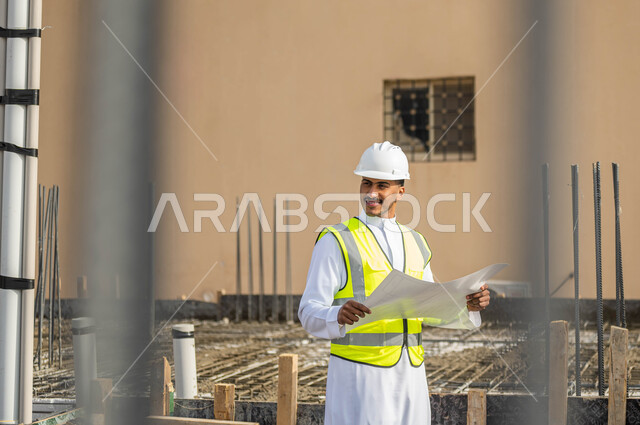 The concept of engineering and construction, supervising the implementation of projects and architectural plans in construction, ensuring good basics for the building, a close-up picture of a Saudi Gulf Arab engineer wearing a helmet and a protective vest, holding a plan in his hand and looking at something, Saudi professions and jobs.