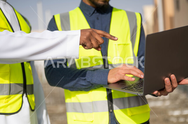 مهن ووظائف سعودية، ارتداء اللباس الخاص بالعمل، الاشارة إلى جهازالحاسوب المحمول و الاطلاع على تصاميم هندسية جديدة، دمج العمل مع التقنية و التكنولوجيا ،صورة مقربة لمهندسان معماريان عربيان خليجيان سعوديان ،العمل في مجال الهندسة المعمارية