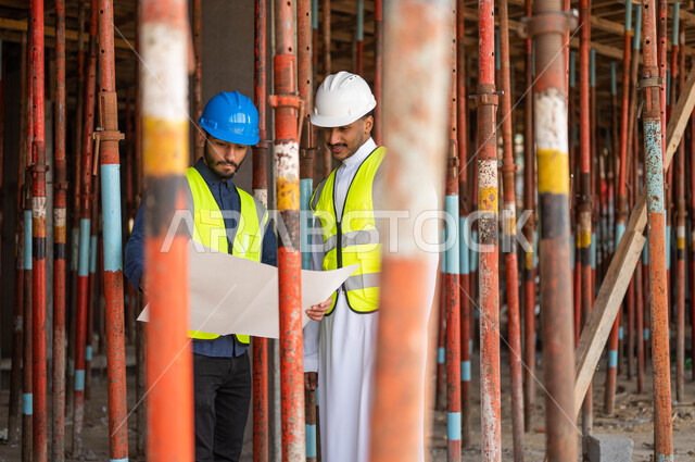 الأحاديث والدردشات التي تدور حول المشروع بإيماءات السرور، عامل ومهندس معماري عربيان خليجيان سعوديان يرتديان الخوذة وسترة الحماية يعملان في مجال الهندسة المعمارية ،الاشراف على تطبيق الخطط و المشاريع الهندسيه في السعودية، الحرص على وضع الأساسيات الجيده في المبنى