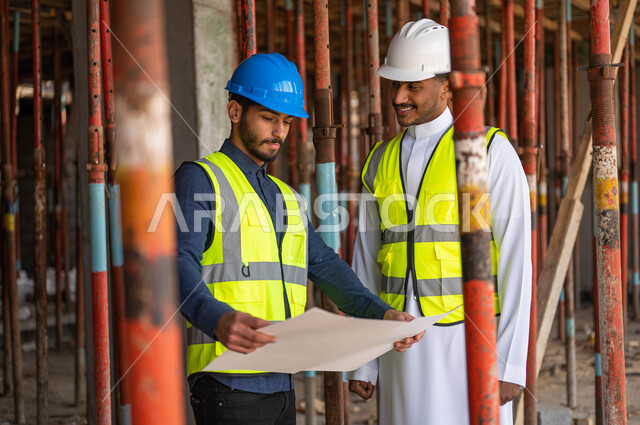 تبادل الأحاديث والدردشات حول المشروع بإيماءات السرور، عامل ومهندس معماري عربيان خليجيان سعوديان يرتديان الخوذة وسترة الحماية يعملان في مجال الهندسة المعمارية ،الاشراف على تطبيق الخطط و المشاريع الهندسيه في السعودية، الحرص على وضع الأساسيات الجيده في المبنى