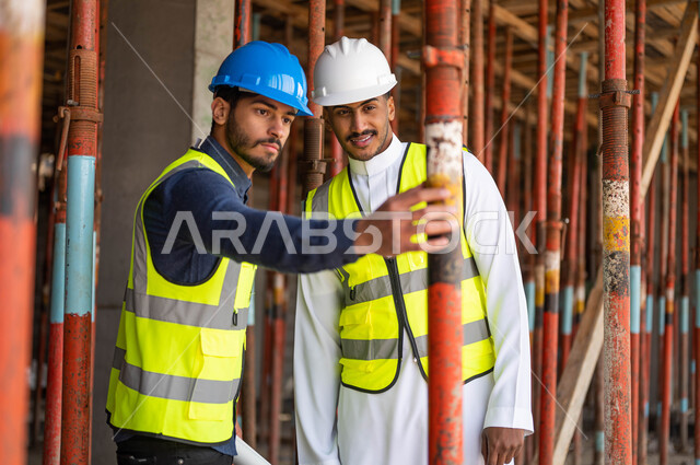 الحرص على وضع الأساسيات الجيده في المبنى ،التشييك على جودة المواد الأولية للبناء، عامل ومهندس معماري عربيان خليجيان سعوديان يرتديان الخوذة وسترة الحماية يعملان في مجال الهندسة المعمارية ،الاشراف على تطبيق الخطط و المشاريع الهندسيه في السعودية
