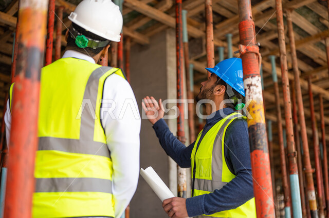 الدردشة والحوارات حول المشروع واقتراح فكر جديدة، عامل ومهندس معماري عربيان خليجيان سعوديان يرتديان الخوذة وسترة الحماية يعملان في مجال الهندسة المعمارية ،الاشراف على تطبيق الخطط و المشاريع الهندسيه في السعودية ، الحرص على وضع الأساسيات الجيده في المبنى