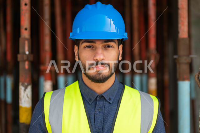 الخطط و المشاريع الهندسيه المعمارية في موقع العمل ،التطور والنمو العمراني على أيدي أبناء الوطن، صورة مقربة لمهندس عربي خليجي سعودي مبتسم يرتدي الخوذة وسترة الحماية ينظر إلى الكاميرا بإيماءات السرور، العمل في القطاع الهندسي