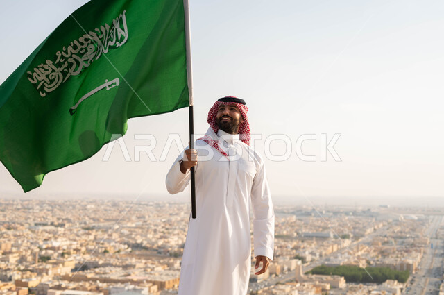 النظر إلى علم المملكه بحب، خلفية أحياء وشوارع مدينة الرياض ،المناسبات والاعياد الوطنية في 8 ربيع الاول، الولاء والاخلاص للوطن، ذكرى اليوم الوطني السعودي 23 سبتمبر، صورة مقربة لرجل عربي خليجي سعودي مبتسم يرتدي الشماغ والزي التقليدي يحتفل بيوم العلم 11 مارس .