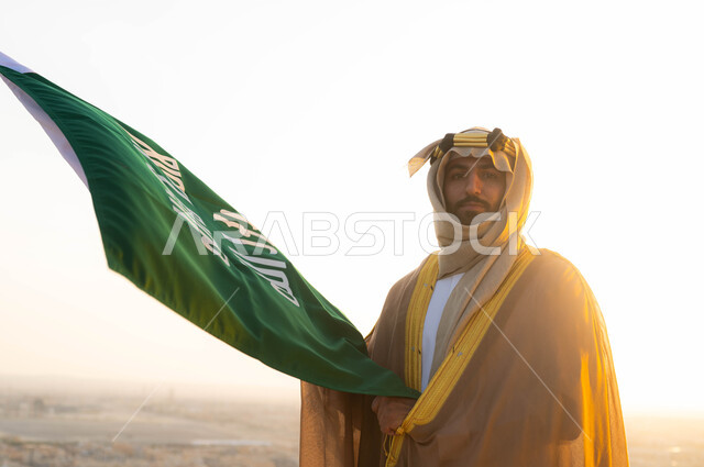 Commemorating the unification of the country in 1727 AD, preserving national identity and pride in its heritage, commemorating the founding day on February 22, traditional folk costume in the central region, the founder of the first Saudi state, Imam Muhammad bin Saud, a Saudi Gulf Arab gentleman wearing a bisht and ghutra, holding in his hand the founding flag.