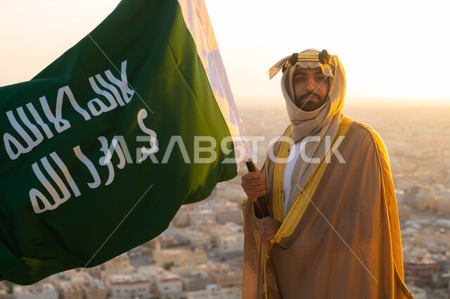 تاريخ توحيد البلاد في 1727 م، الحفاظ على الهوية الوطنية والفخر بتراثها ،ذكرى يوم التأسيس في 22 شباط، الزي الشعبي التقليدي في المنطقة الوسطى ، مؤسس الدولة السعودية الاولى الامام محمد بن سعود, سيد عربي خليجي سعودي يرتدي البشت والغترة يحمل بيده علم التأسيس 